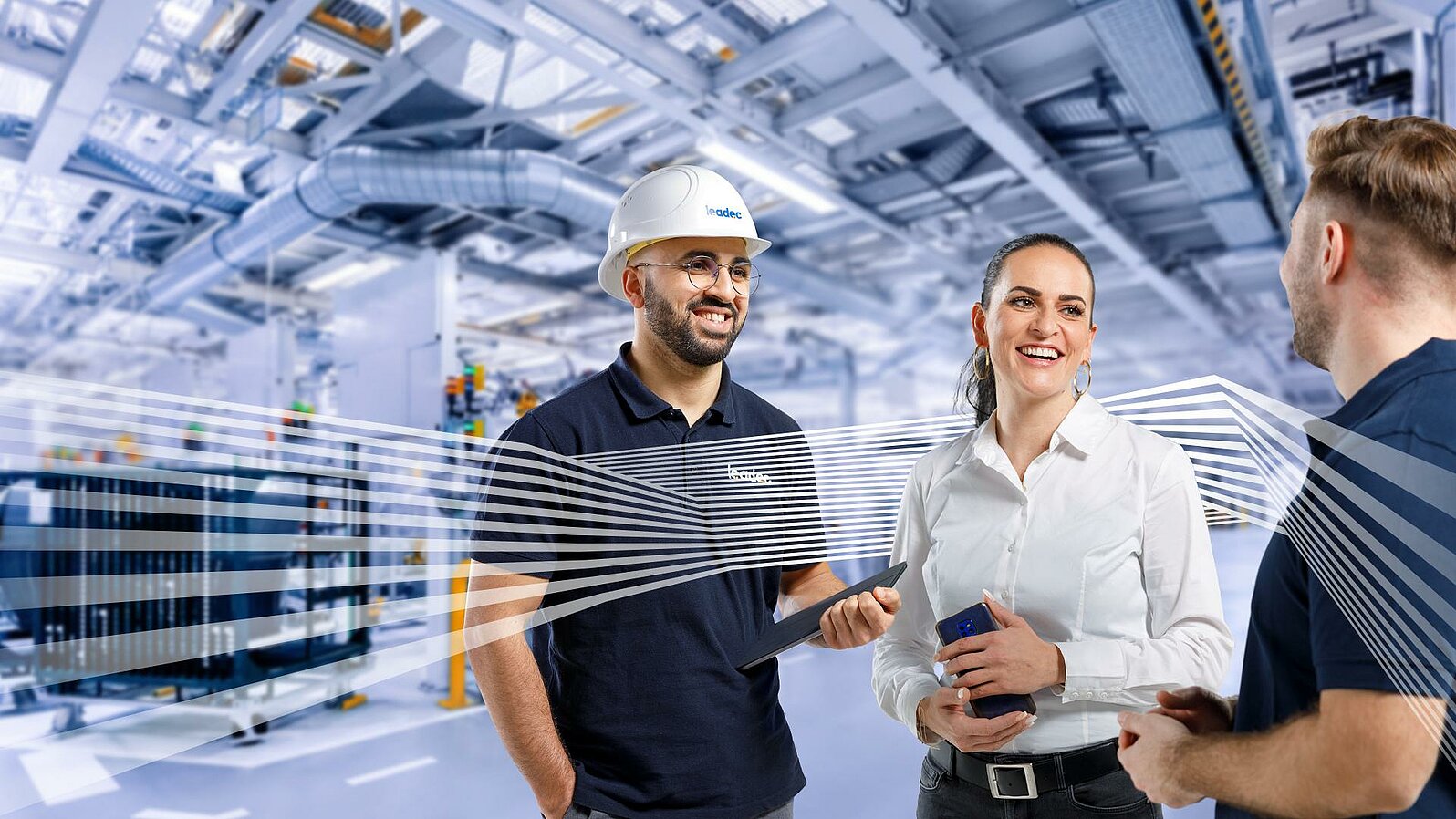 Three Leadec employees in workwear talking in front of a factory background.