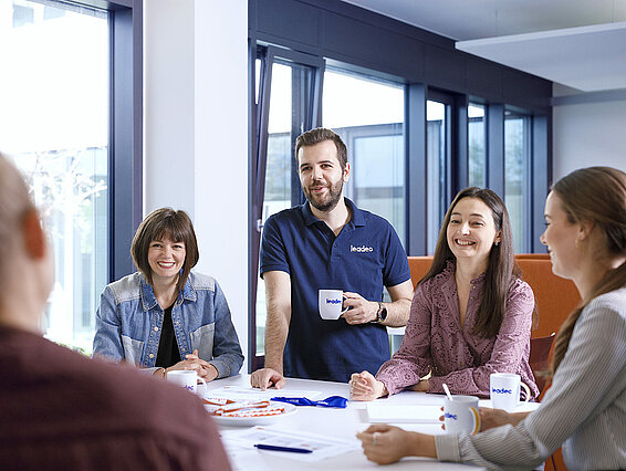 Eine Gruppe von Leadec-Mitarbeitenden, die um einen Tisch im Büro herumstehen und sich unterhalten.