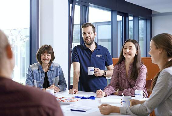 A group of Leadec employees standing around a table having a conversation in the office. 