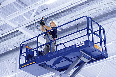 Leadec employee on a scissor lift installing media supply on the ceiling of a factory.