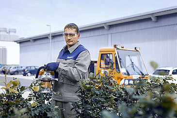 A Leadec employee cutting the hedge with a chainsaw at a factory site.