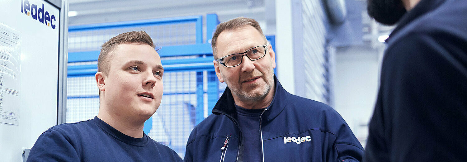 Two Leadec employees inspecting machines and operating equipment in a production. 