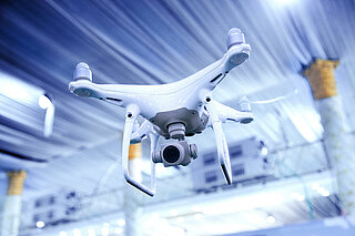 White drone flies under the ceiling in a production hall.