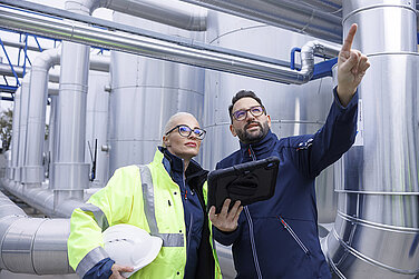 A female and a male Leadec employee with a tablet inspecting pipes on a factory roof.