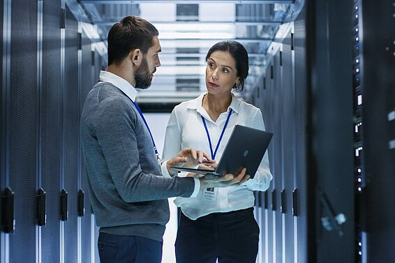 Mann und Frau mit einem Laptop im Serverraum. 